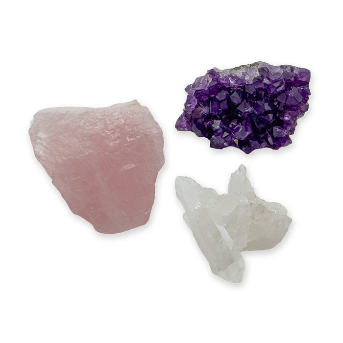 Raw crystal set trio: a raw rose quartz chunk, an amethyst cluster from Uruguay and a clear quartz cluster from Brazil, together on white