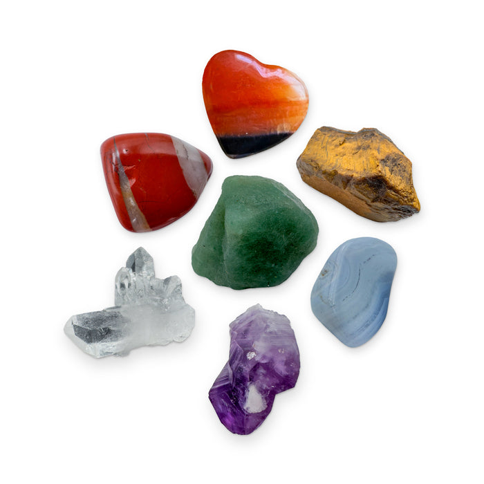 Seven Chakra Crystal Kit: red jasper, carnelian heart, tiger eye, green aventurine, blue lace agate, amethyst point and clear quartz cluster, shown together on white