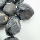 Set against a soft backdrop is an Apache Tear stone, shown at hand scale.