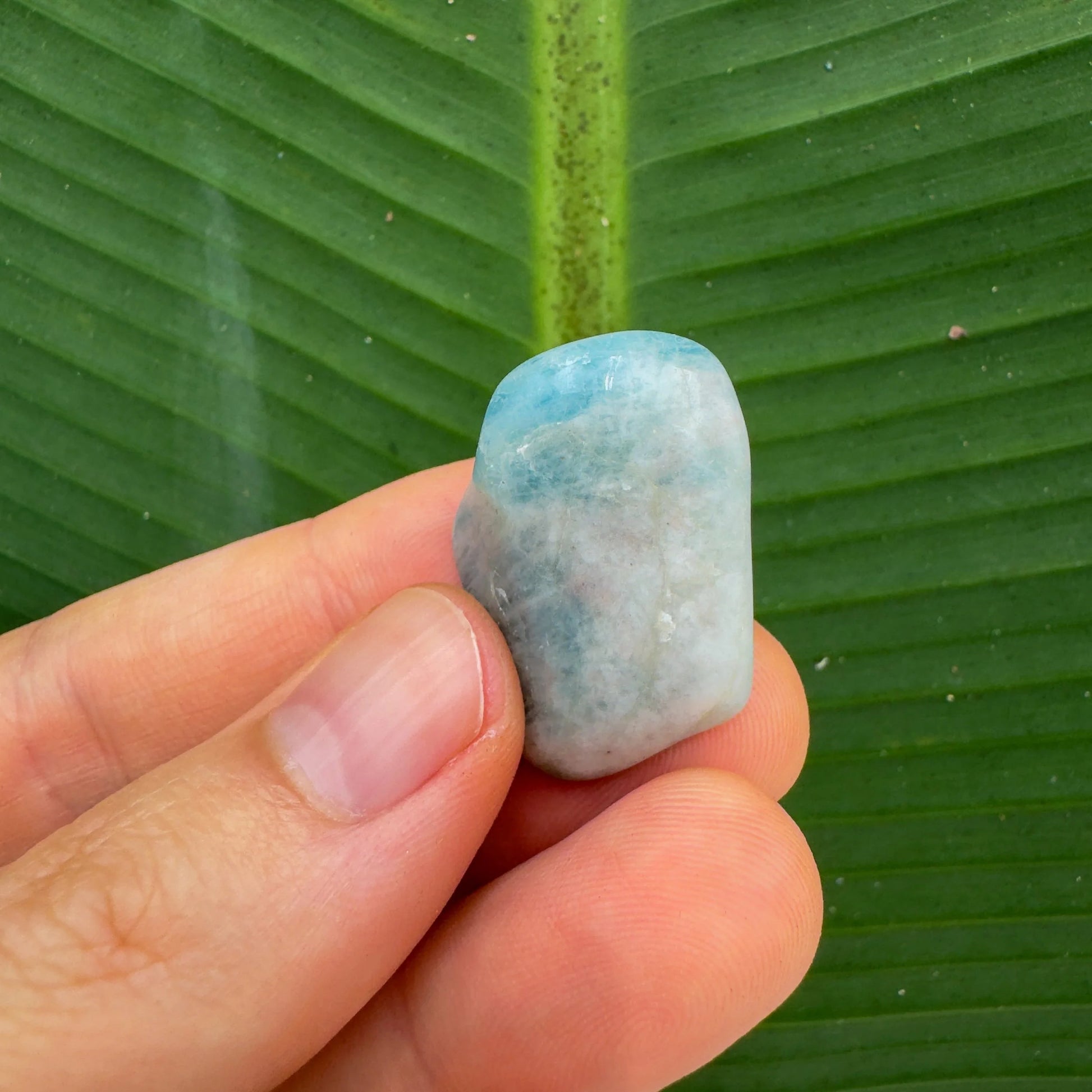 Hand-scale shot of a Aquamarine tumbled stone often kept for Stress Relief.