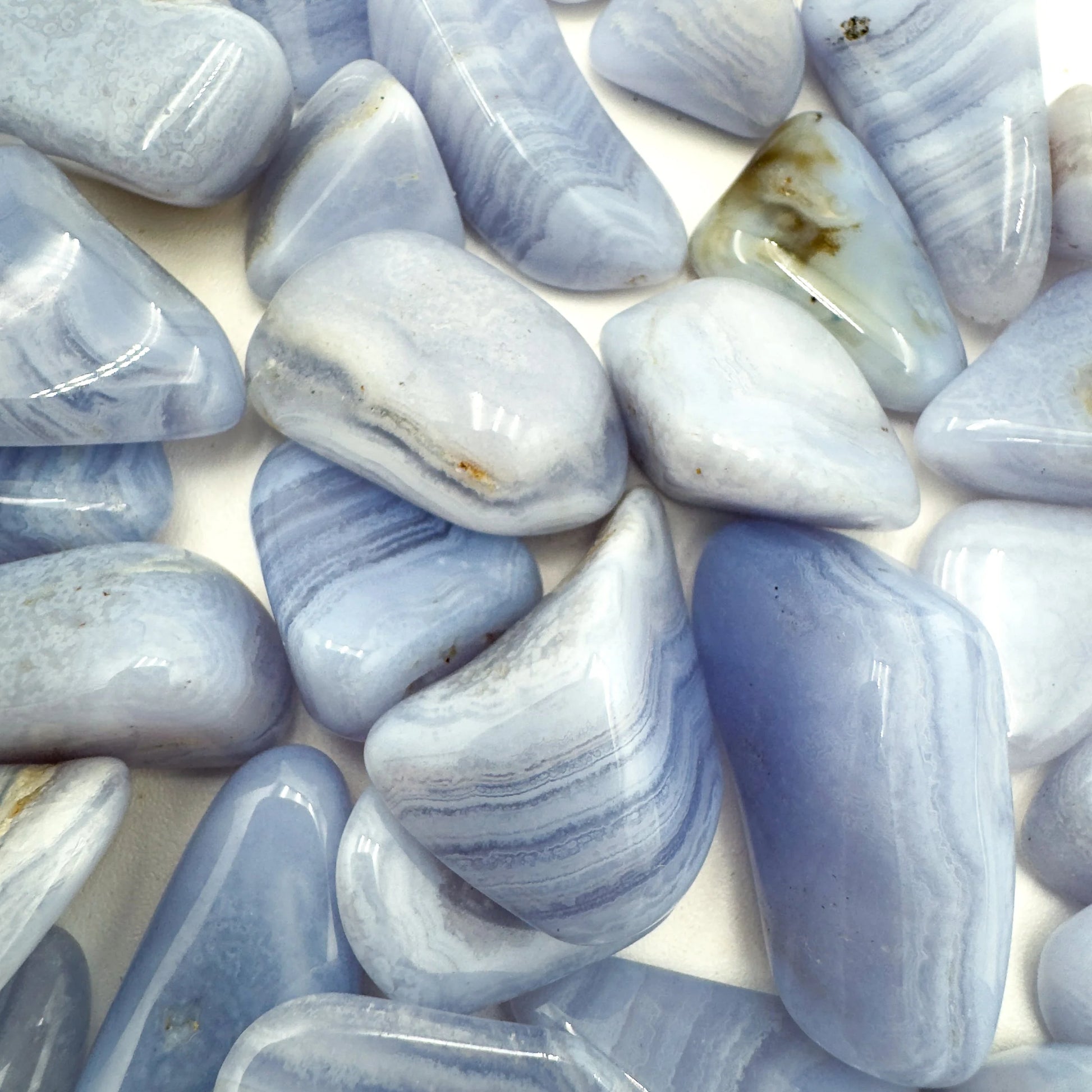 Hand-scale shot of a Blue Lace Agate tumbled stone held against natural backdrop.