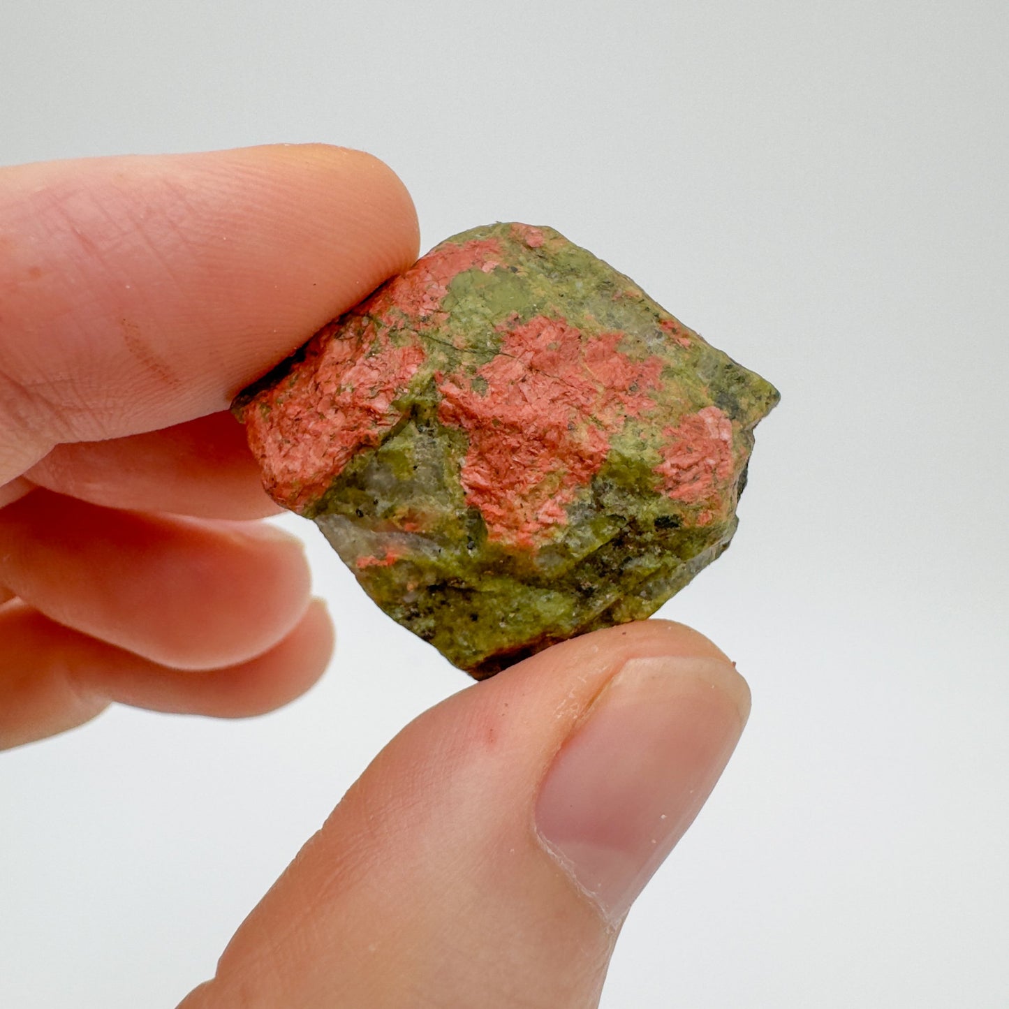 Holding an Unakite raw crystal, with hand-sized presence.