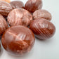 Side-on view of Grade AAA Red Aragonite tumbled stone, showing natural texture, for Energy.