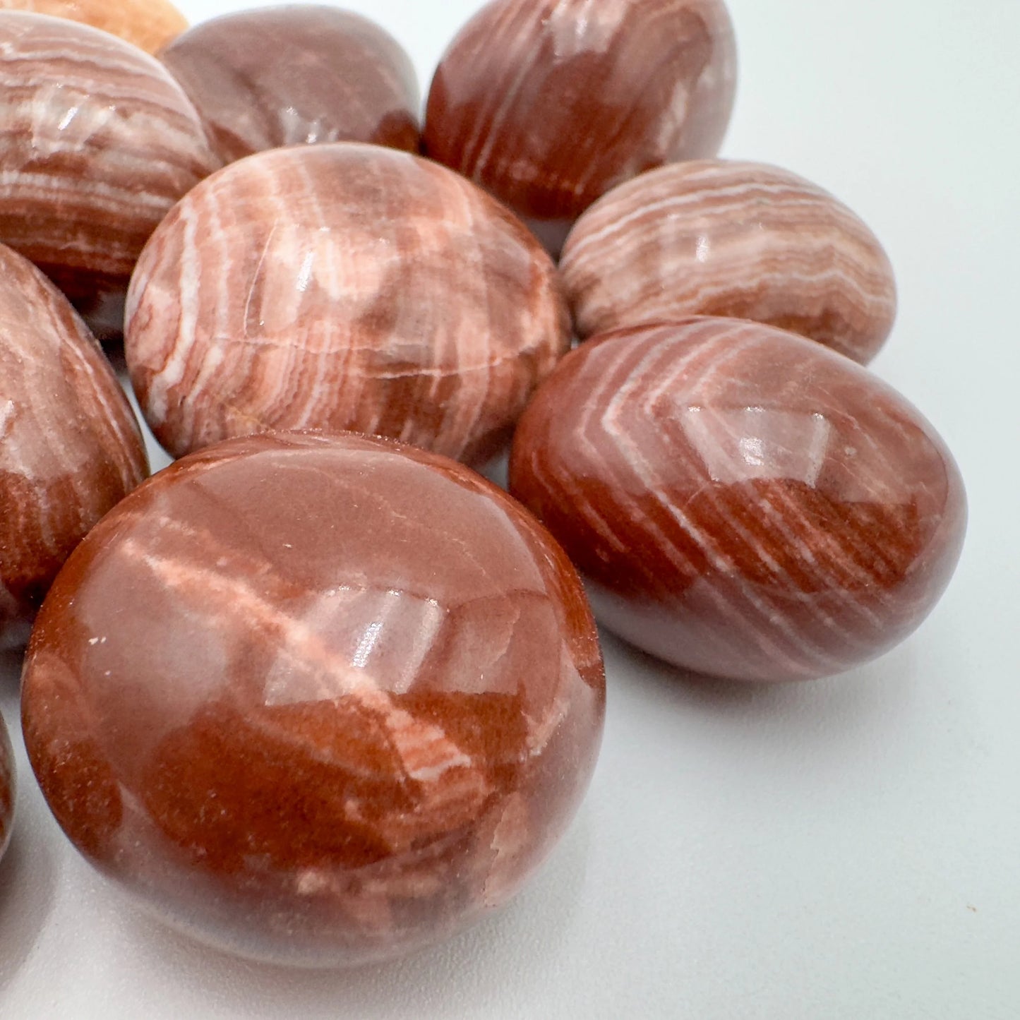 Side-on view of Grade AAA Red Aragonite tumbled stone, showing natural texture, for Energy.