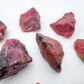 Three-quarter view of Rhodonite raw crystal, set against a soft neutral surface.