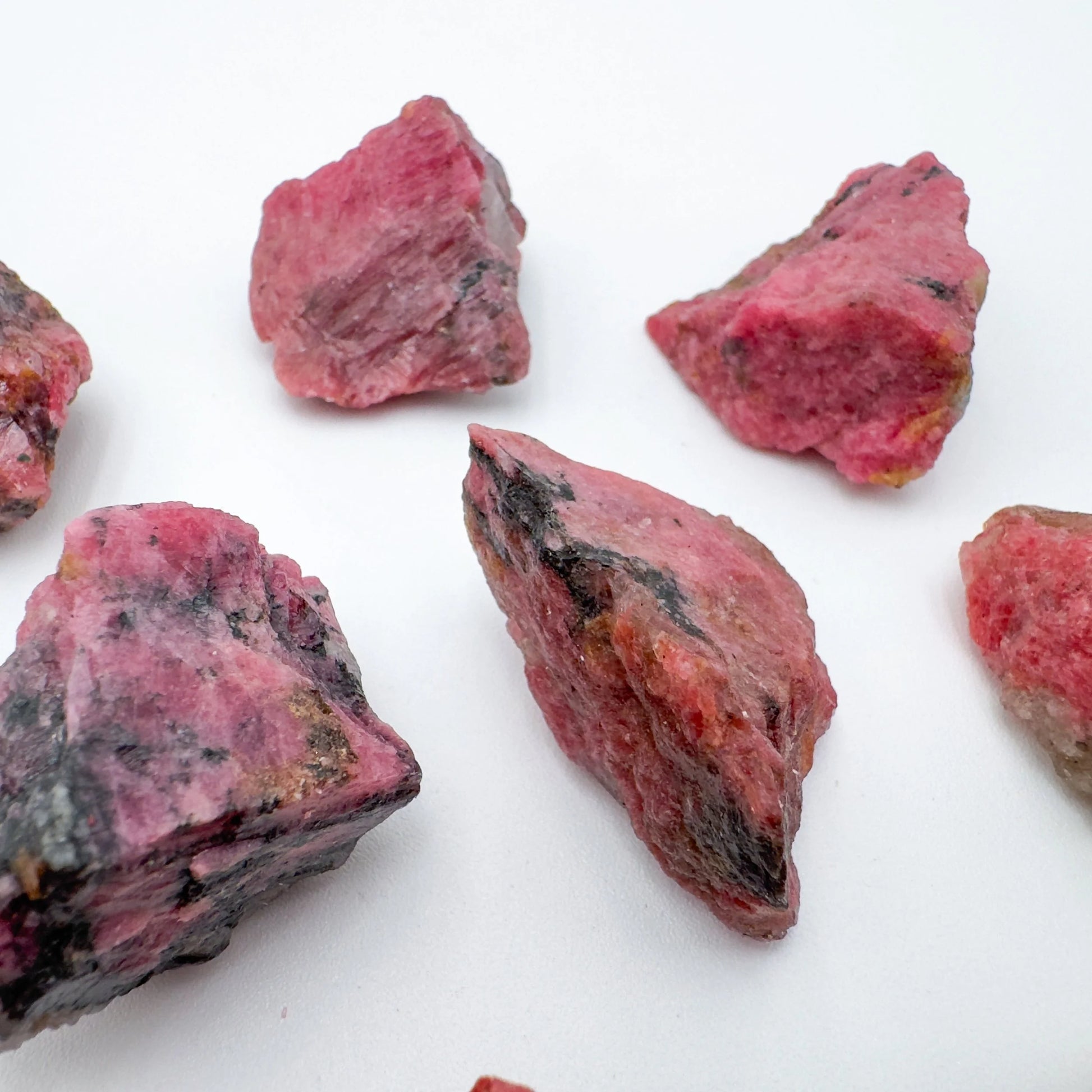 Three-quarter view of Rhodonite raw crystal, set against a soft neutral surface.