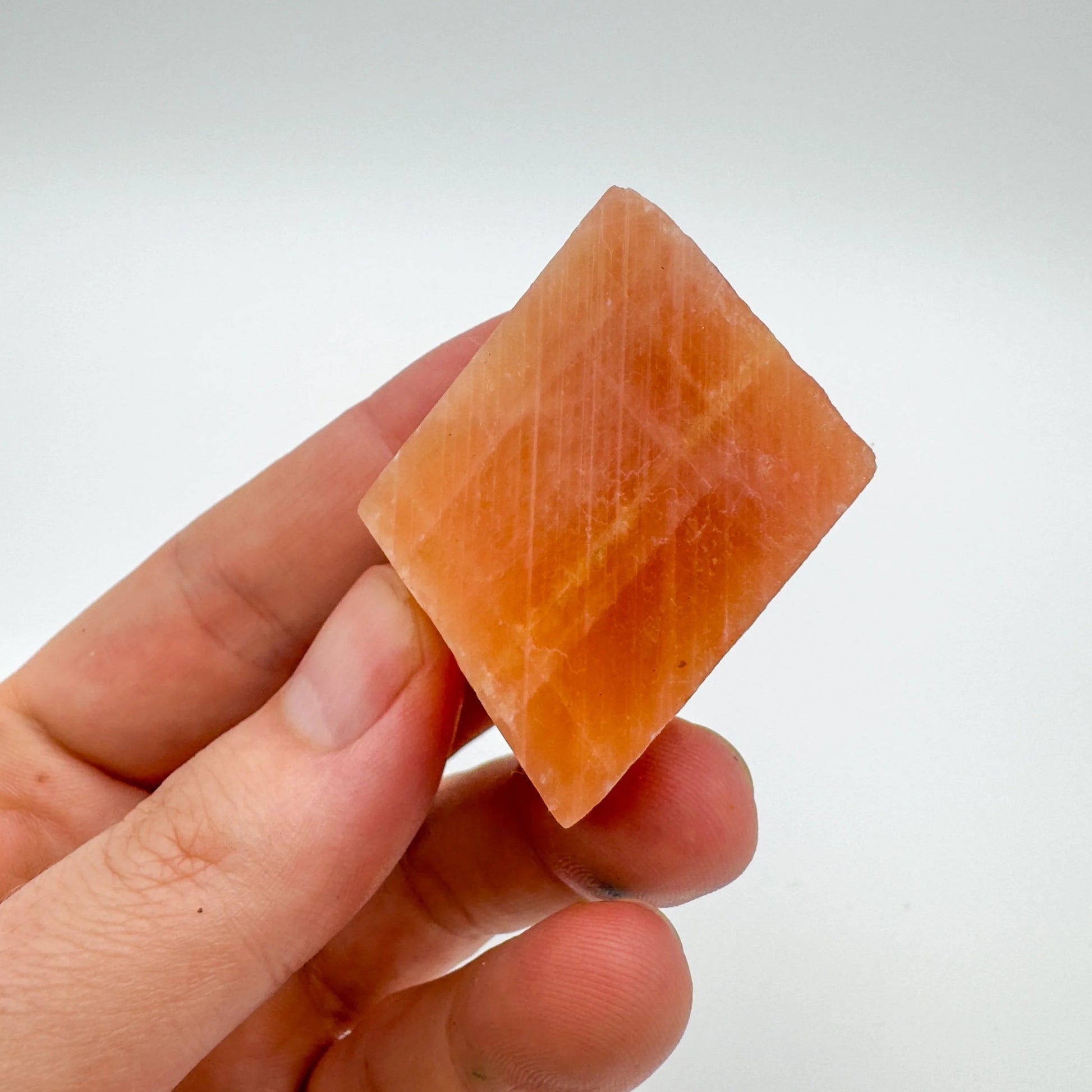 Scale reference of a Orange Calcite raw stone held against natural backdrop.