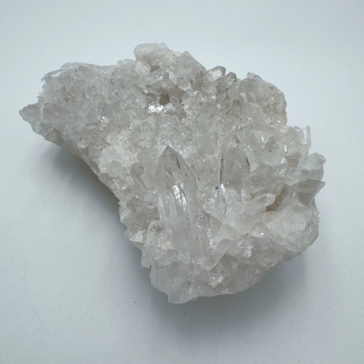 Holding a Clear Quartz specimen, from Rio Grande do Sul, Brazil, set against a soft neutral surface.