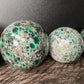 Held against neutral backdrop is an Emerald stone, from Midlands Province, Zimbabwe, linked to Love, captured in natural daylight.