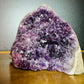 Palm-scale view of a Amethyst raw geode held against natural backdrop.