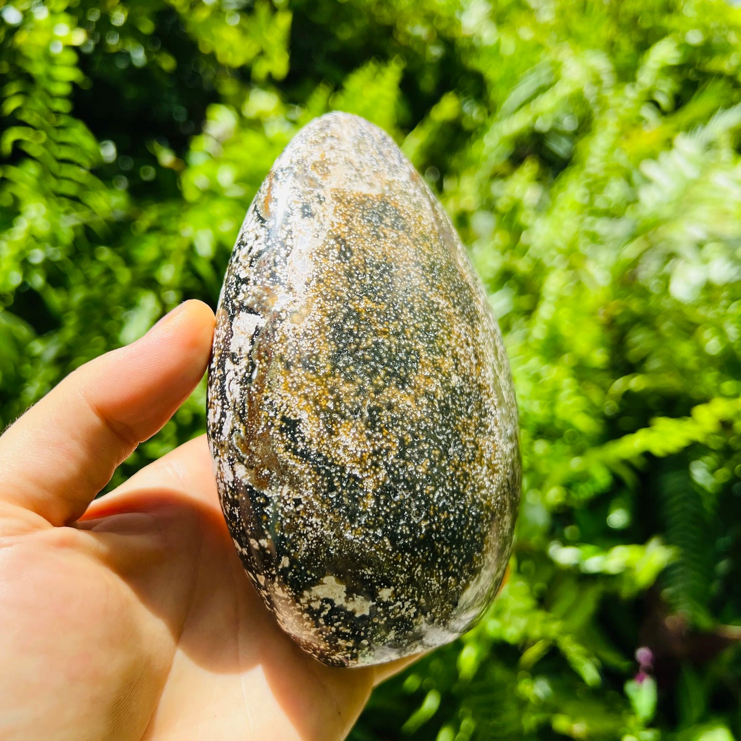 Held in palm of an Ocean Jasper stone, traditionally used for Emotional Healing, with natural details visible.