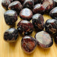Near view of Grade AAA Garnet tumbled stone, linked to Energy.