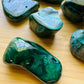 Lifestyle view of a Malachite tumbled stone held against natural backdrop.