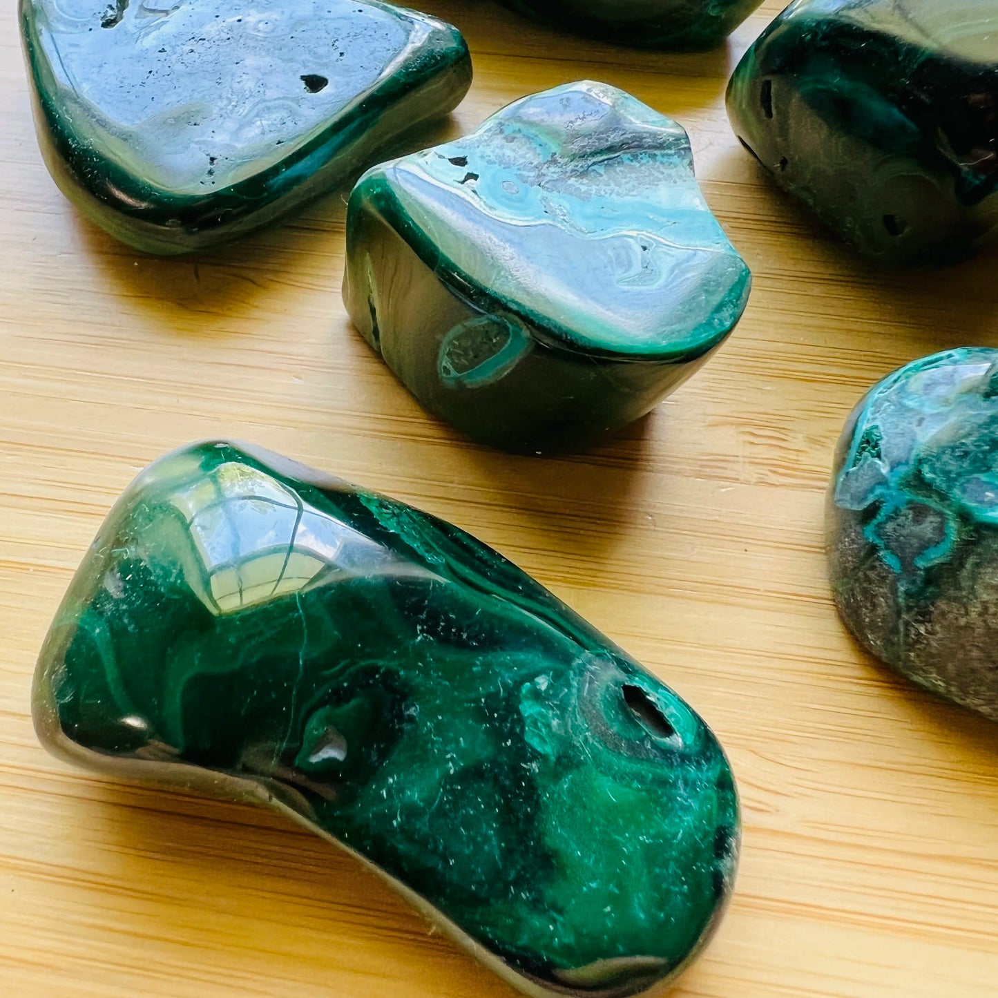 Lifestyle view of a Malachite tumbled stone held against natural backdrop.