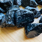 Hand-held view of a Snowflake Obsidian raw stone held against natural backdrop, United States-sourced.