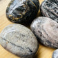 Side-on view of Black Moonstone palm stone, Madagascar-sourced, showing natural inclusions.