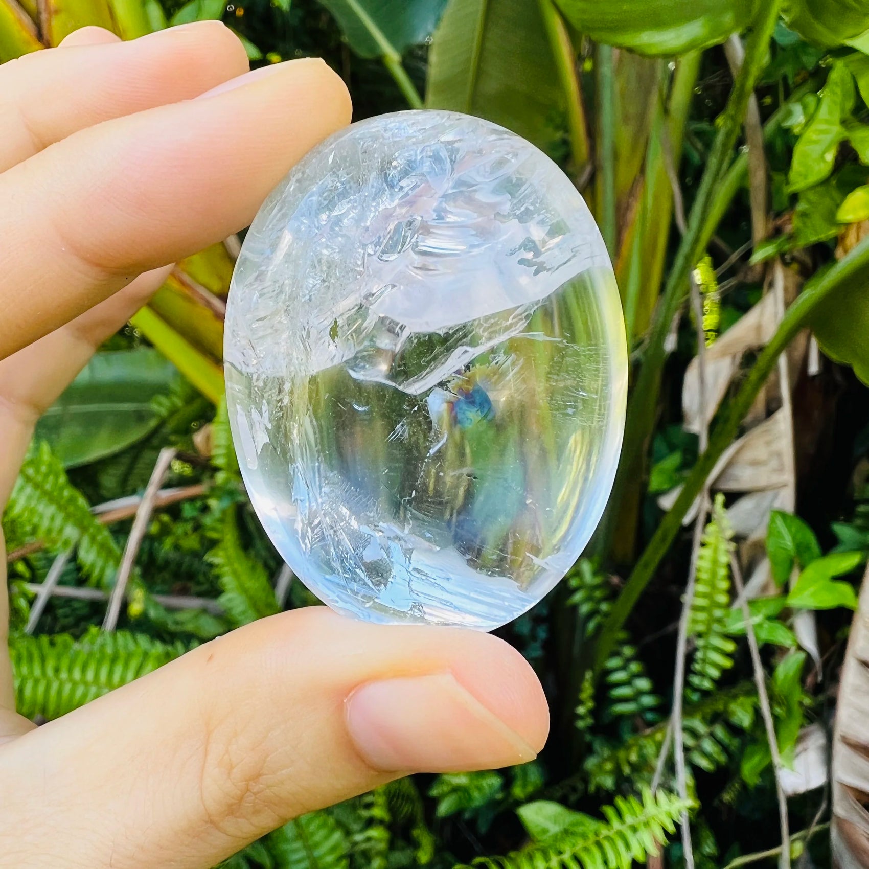 Set against a soft backdrop is a Clear Quartz palm stone, from Vakinankaratra, Madagascar, showing the piece in repose.