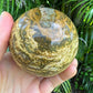 Hand-scale shot of a Ocean Jasper polished sphere held against natural backdrop.