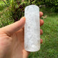 Hand-held view of a Selenite polished cylinder held against natural backdrop.