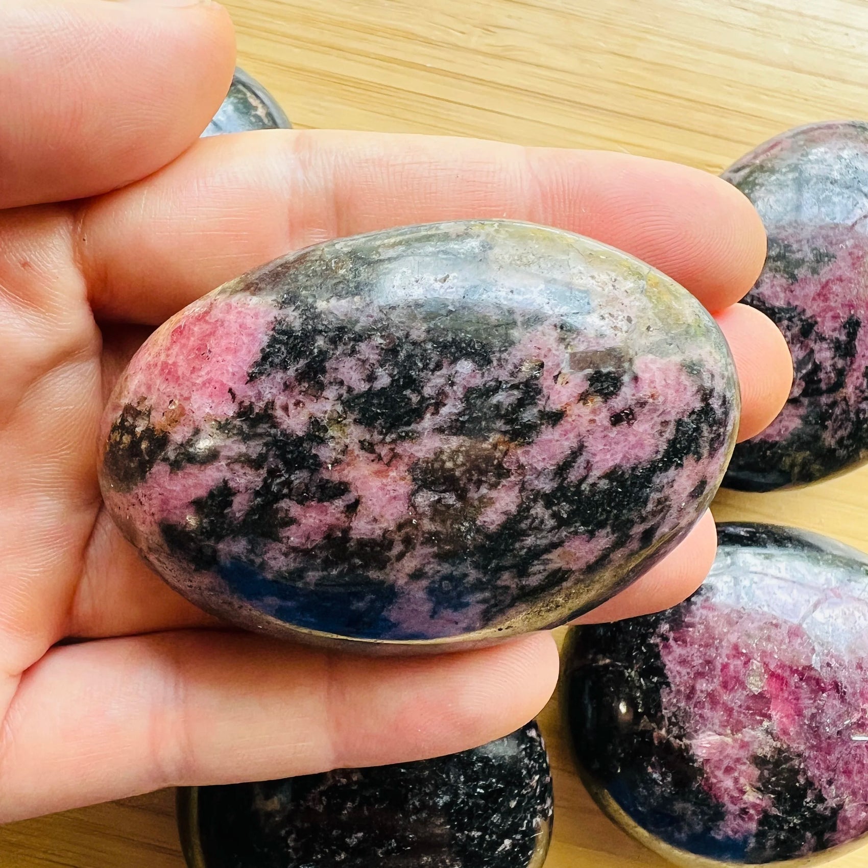 Resting display of Rhodonite palm stone, captured in soft, even lighting.