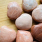 In-hand view of a Peach Moonstone polished heart held against natural backdrop.