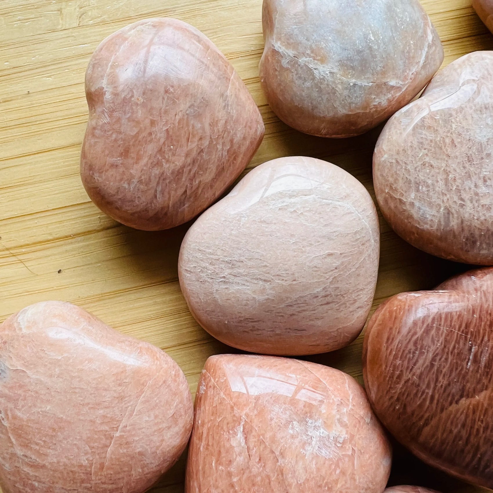 In-hand view of a Peach Moonstone polished heart held against natural backdrop.