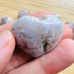 Held against neutral backdrop is a Flower Agate stone, traditionally used for Grounding, showing natural surface character.