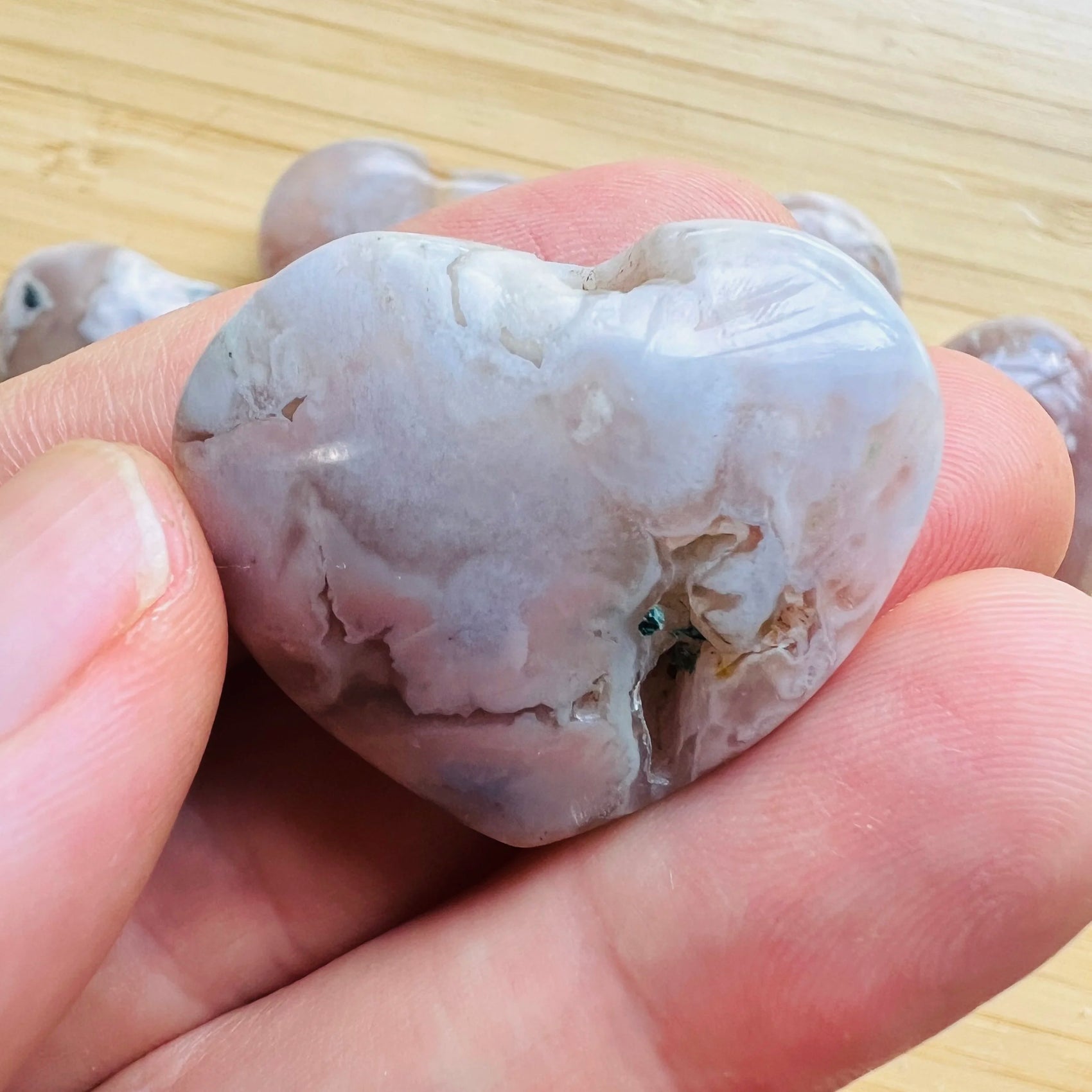 Held against neutral backdrop is a Flower Agate stone, traditionally used for Grounding, showing natural surface character.