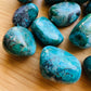 Top-down shot of Chrysocolla tumbled stone, showing earthy tone, sourced from Arequipa, Peru.