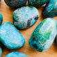 Held in hand, a single Chrysocolla tumbled stone sourced from Arequipa, Peru.