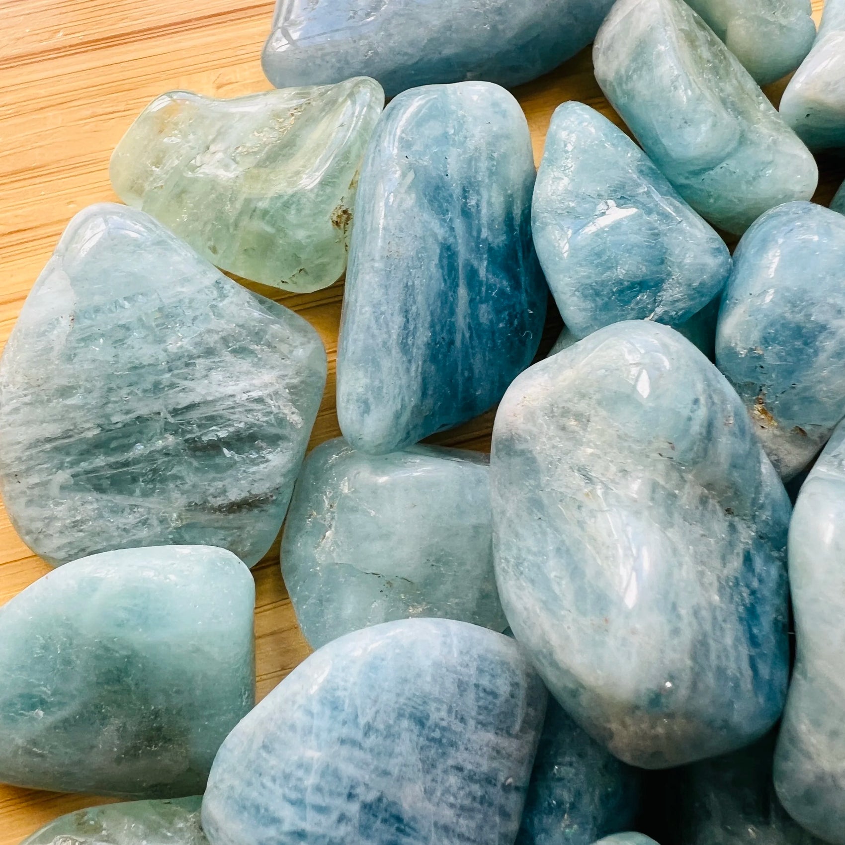 Lifestyle view of a Aquamarine tumbled stone held against natural backdrop, hand-selected from Minas Gerais, Brazil.