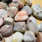 Hand-held view of a Pink Agate tumbled stone often worked with for Love and Self Love, from Botswana.