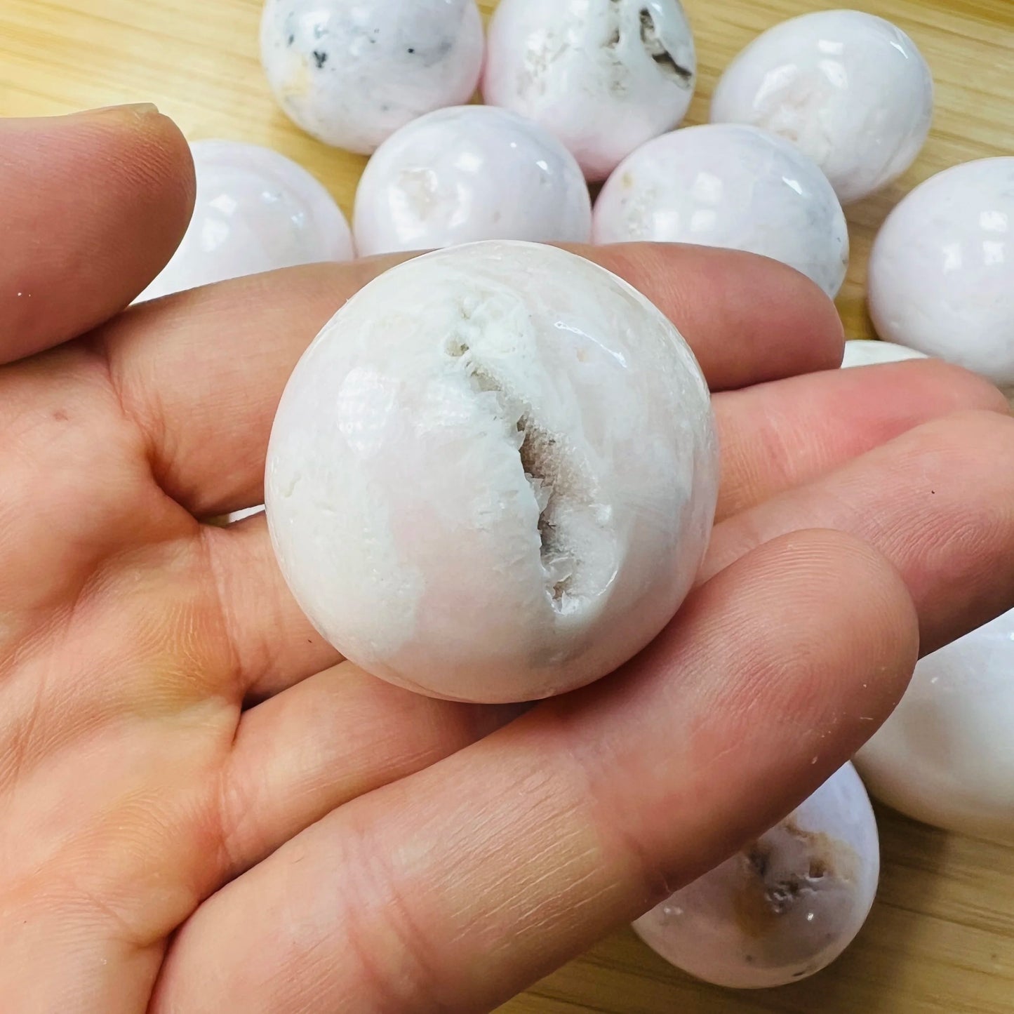 Held against neutral backdrop is a Mangano Calcite tumbled stone, from Ancash, Peru, traditionally used for Stress Relief, showing natural surface character.
