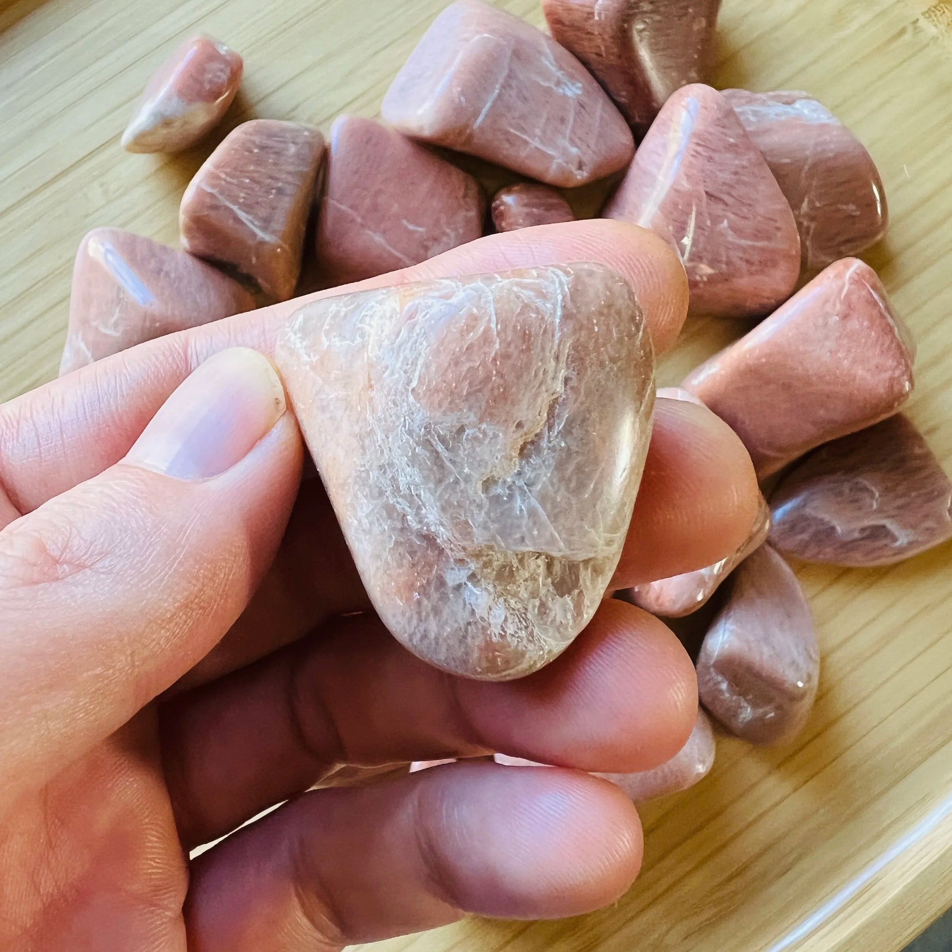 Open-palm view of Peach Moonstone tumbled stone, often kept for Self Love, with character of the piece on display.