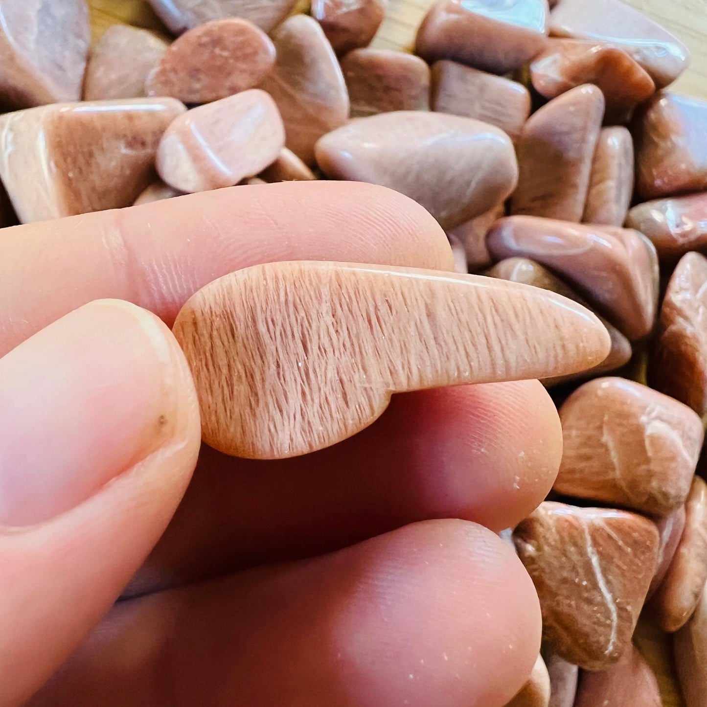 In-hand view of a Peach Moonstone tumbled stone held against natural backdrop.