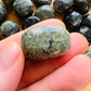 Natural light context of Jade tumbled stone, shown alongside the hand for scale.