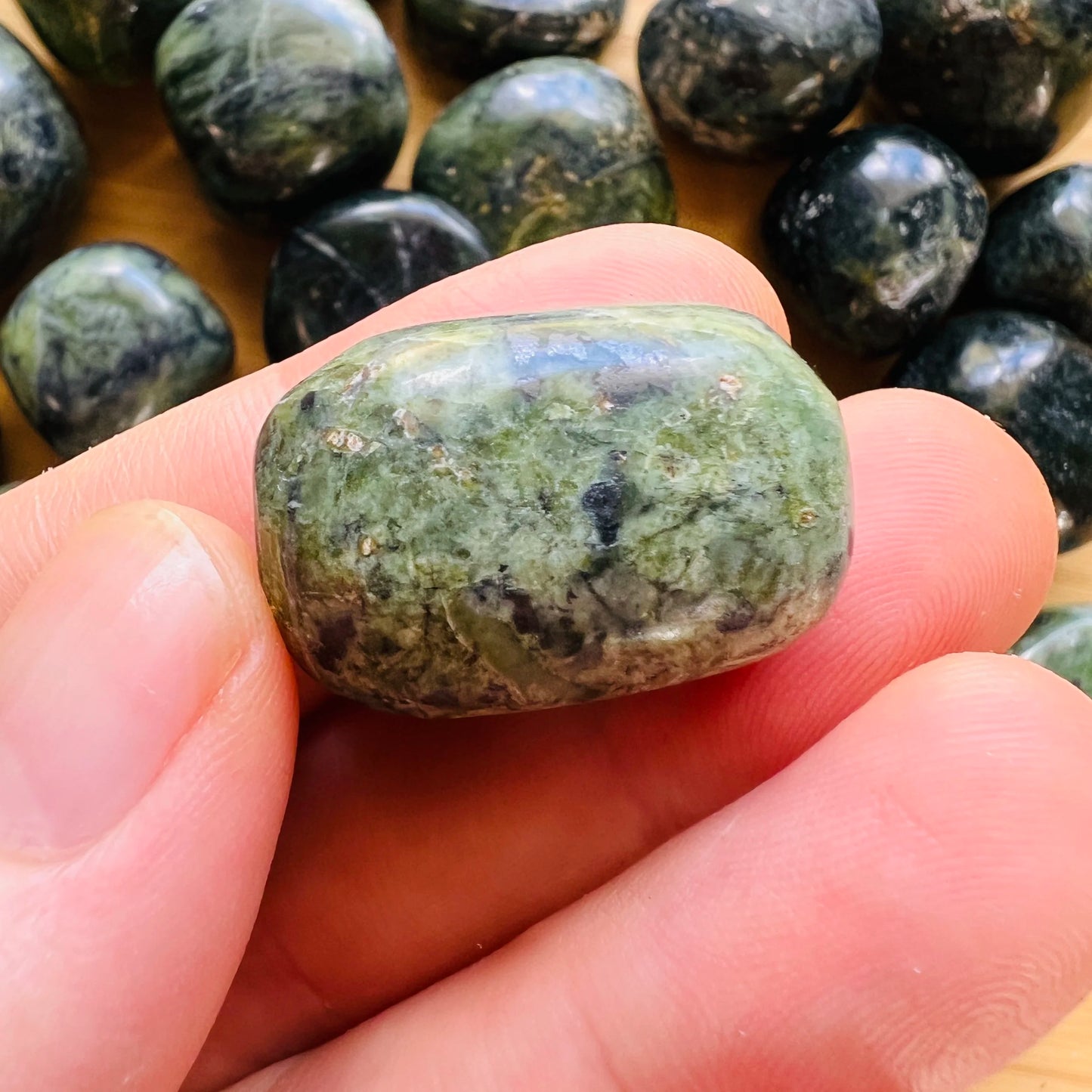 Natural light context of Jade tumbled stone, shown alongside the hand for scale.