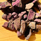Held in hand, a Purpurite raw stone held against natural backdrop, sourced from Erongo, Namibia.