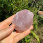 Hand-scale view of Rose Quartz specimen, set against a soft neutral surface.