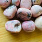 Rear view of Grade AA Rhodonite tumbled stone, showing characteristic color, sourced from Ancash, Peru.