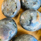 Natural light view of a Labradorite palm stone held against natural backdrop, from Madagascar.
