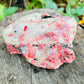 Size comparison with a Rhodonite specimen held against natural backdrop, from Zimbabwe.