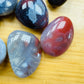 Size comparison with a Red Agate tumbled stone held against natural backdrop.