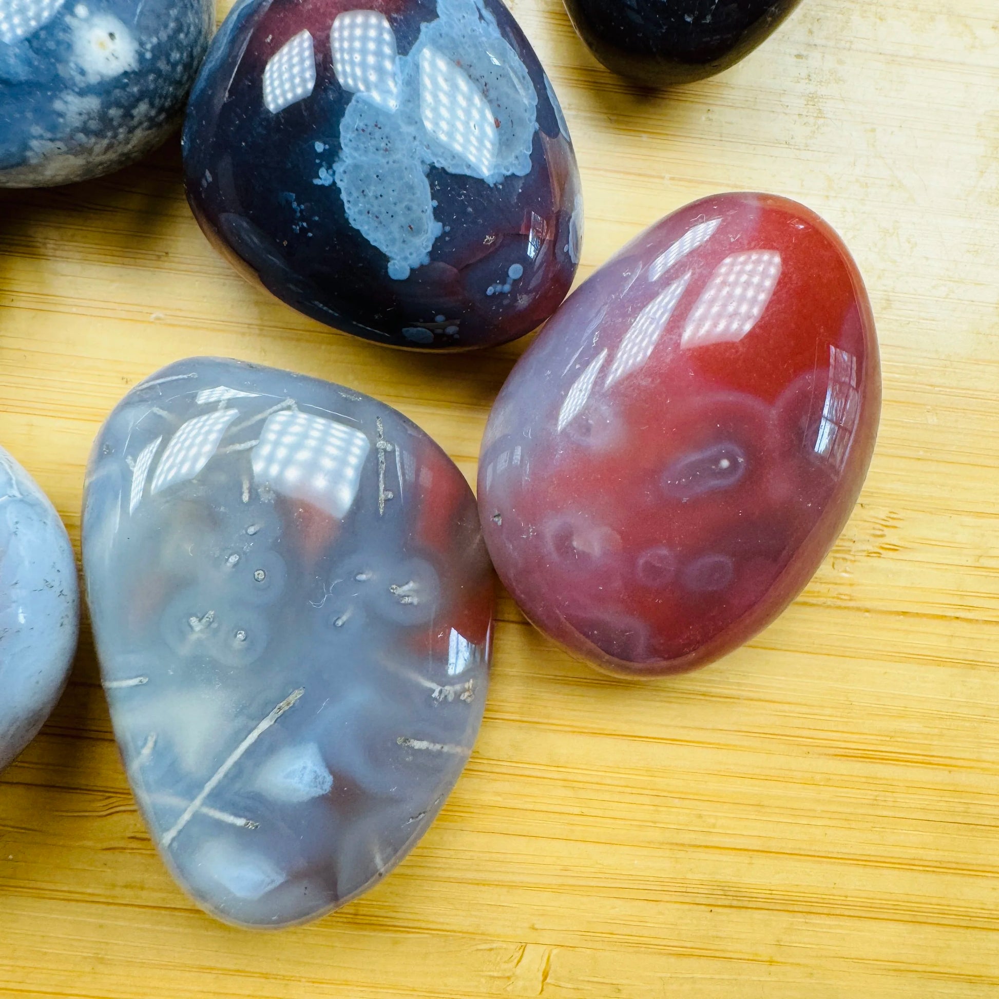 Size comparison with a Red Agate tumbled stone held against natural backdrop.