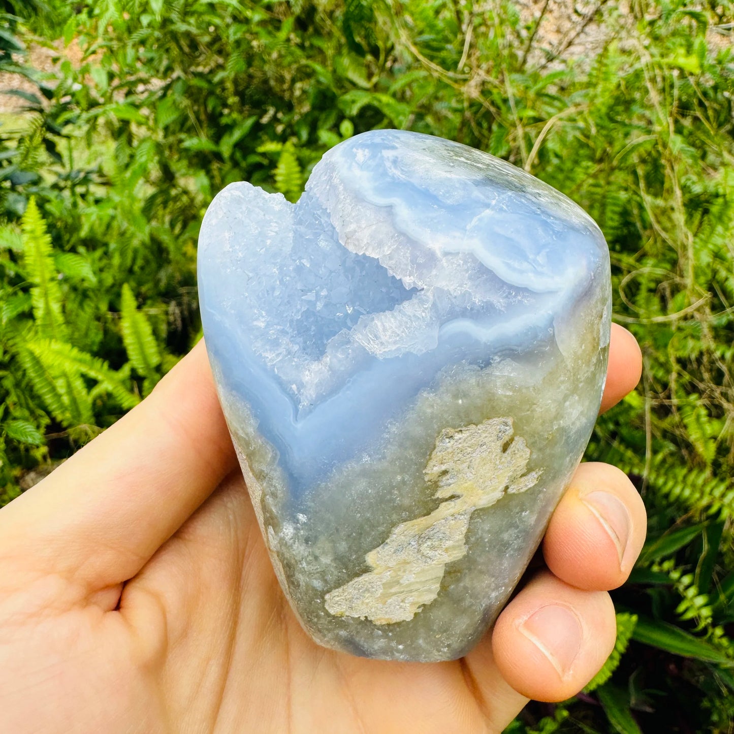 Hand-scale shot of a Blue Lace Agate specimen held against natural backdrop, Malawi-sourced.