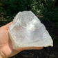 Held in hand, a Selenite specimen held against natural backdrop, sourced from New Mexico, USA.