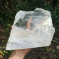 Hand-held view of a Selenite specimen held against natural backdrop.