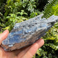 Set against a soft backdrop is a Blue Kyanite specimen, from Minas Gerais, Brazil, traditionally used for Intuition, shown for proportion against the hand.