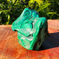 Held in hand is a Malachite specimen, shown for shape and scale.