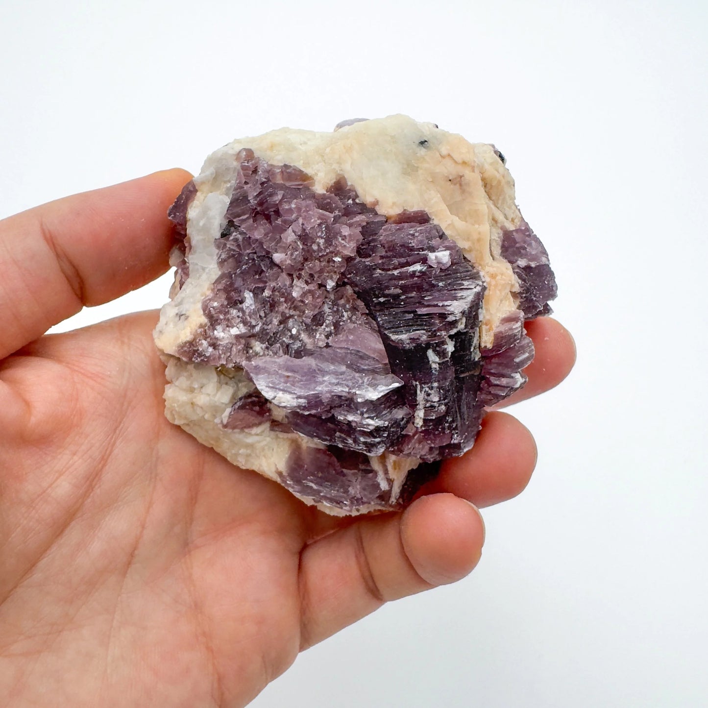 Held against neutral backdrop is a Lepidolite specimen, linked to Self Love, showing the wear and finish.